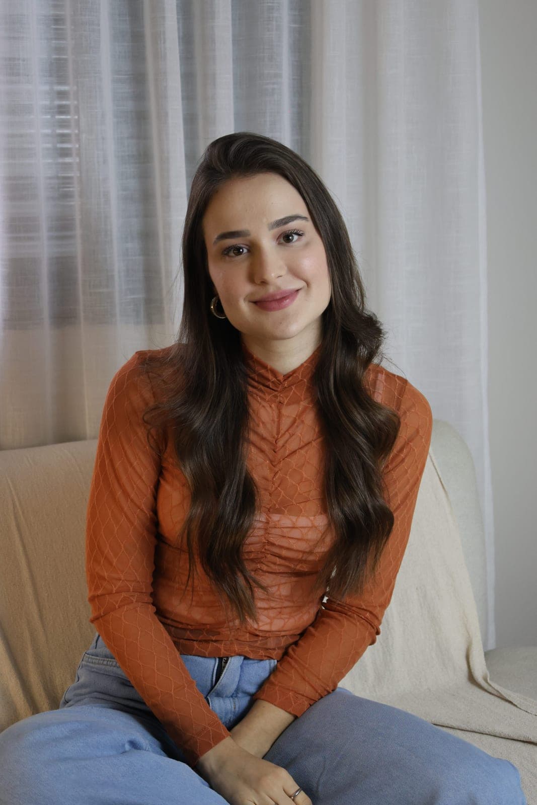 Psicóloga Ana Carolina Crema sentada no sofá, de blusa laranja