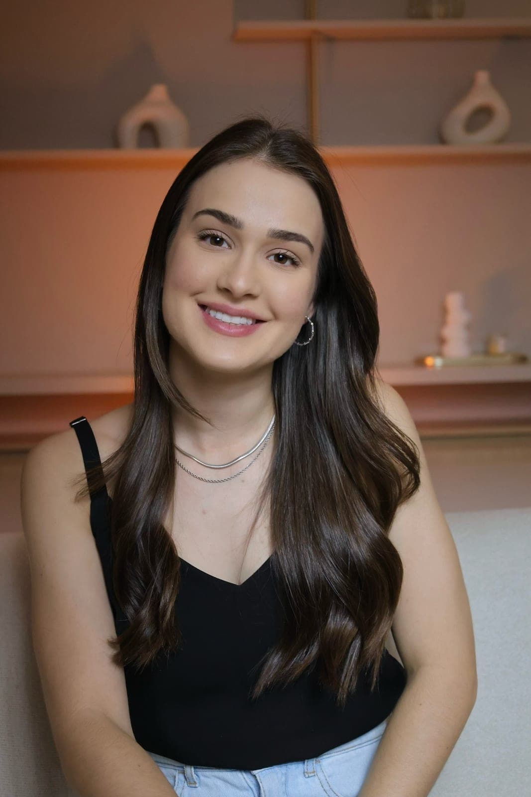 Psicóloga Ana Carolina Crema sentada no sofá, de blusa preta