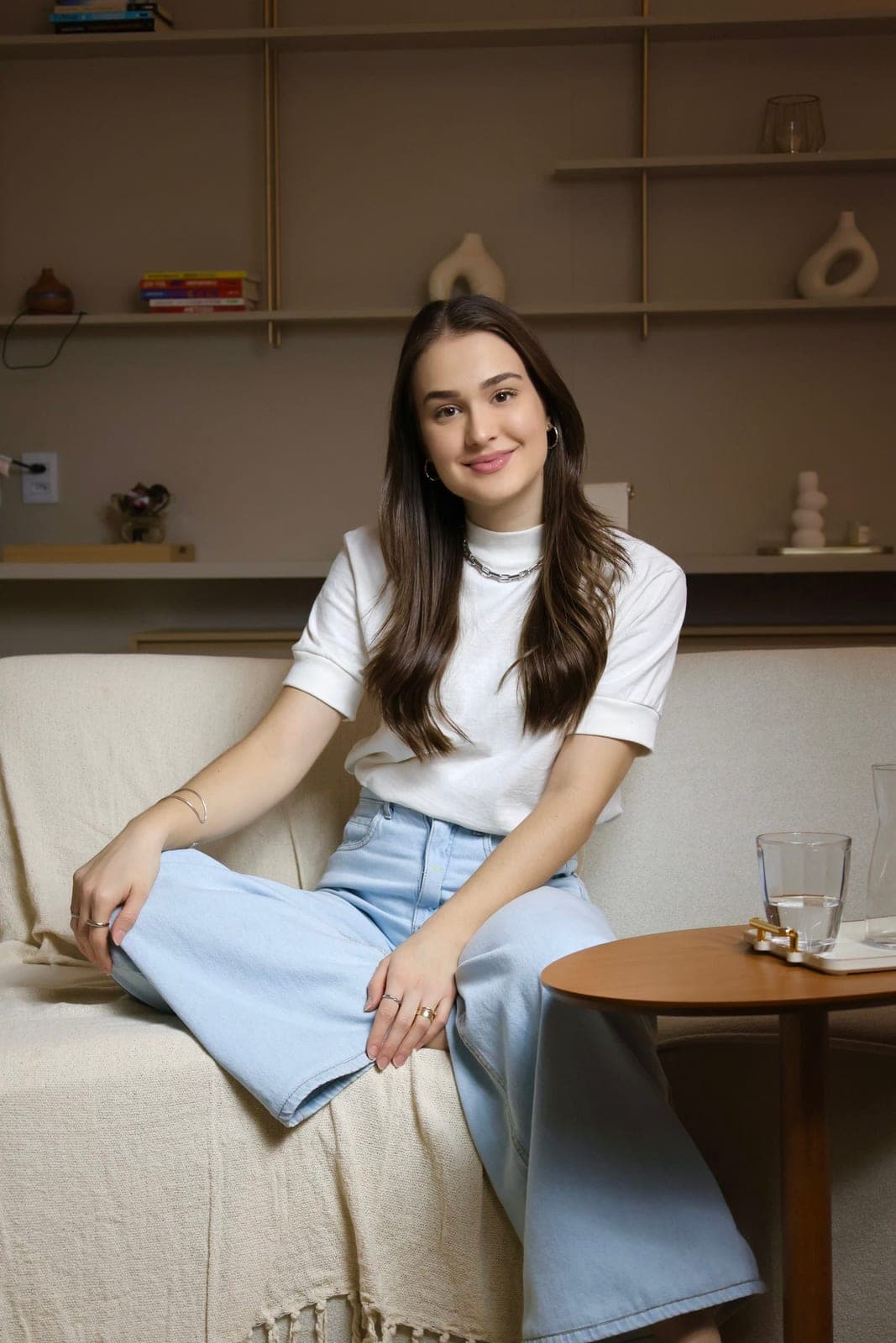 Psicóloga Ana Carolina Crema no consultório, com estante ao fundo