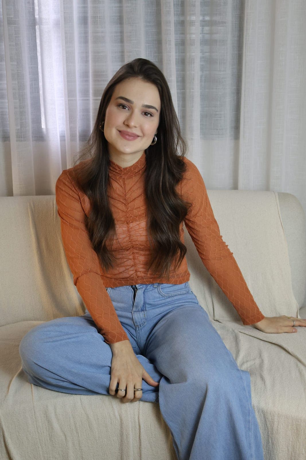 Psicóloga Ana Carolina Crema sentada de forma descontraída no sofá