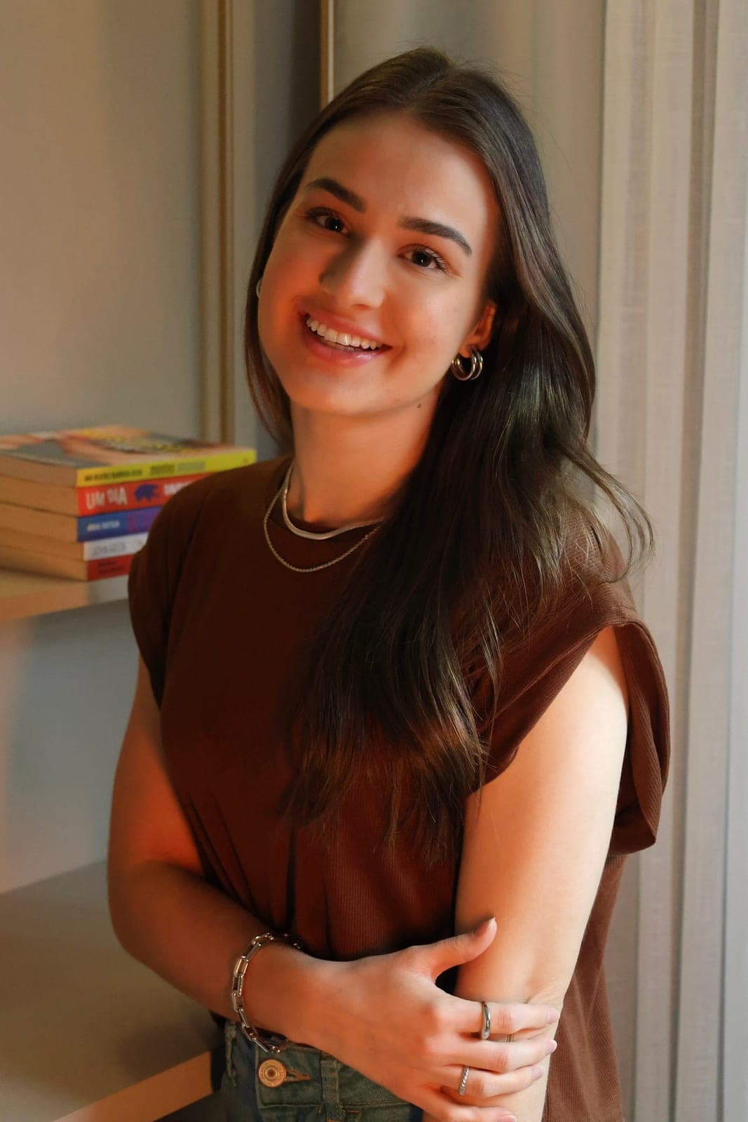 Psicóloga Ana Carolina Crema sorrindo ao lado de livros